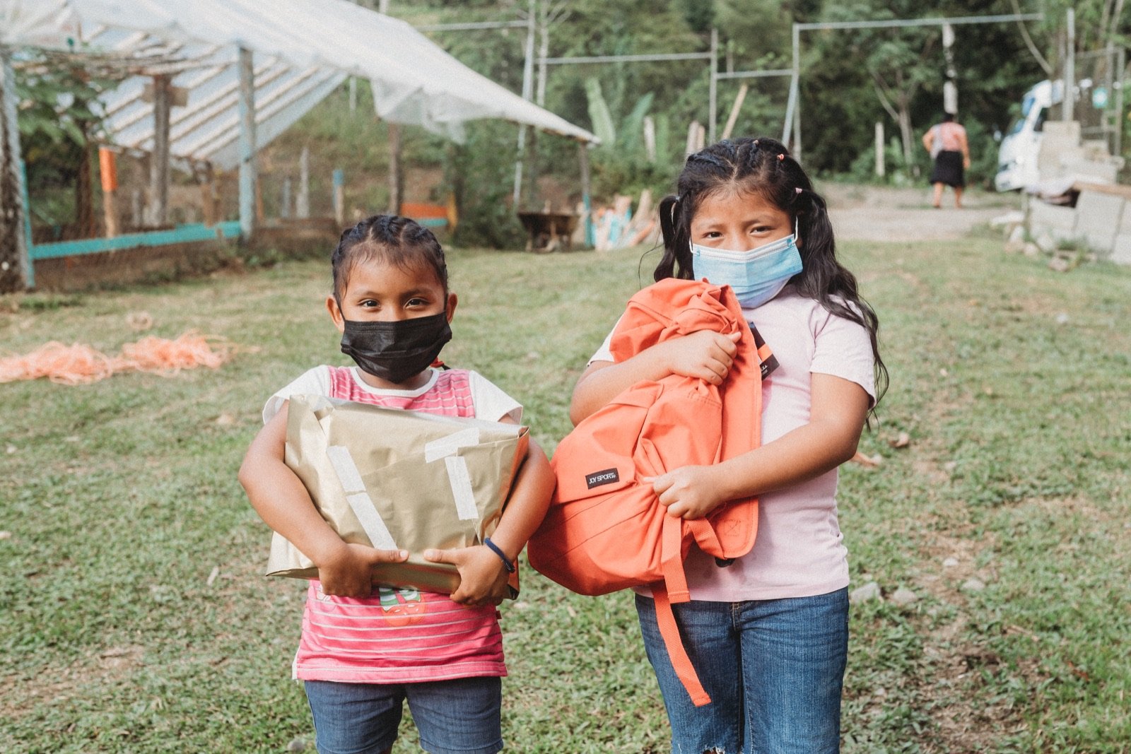 Dos niñas sonríen sosteniendo su mochila y kit escolar recién entregados