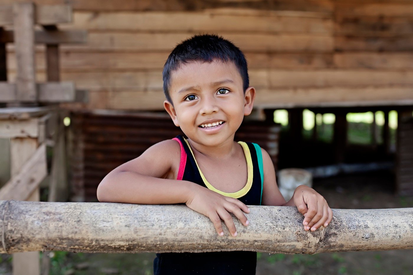 Niño sonriendo apoyado en un barandal de madera